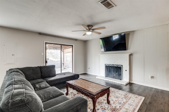 living area featuring visible vents, dark wood-type flooring, a brick fireplace, ceiling fan, and a textured ceiling