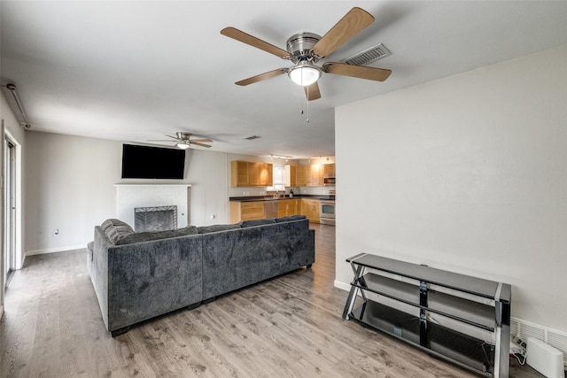 living area featuring light wood-style floors, baseboards, a fireplace, and visible vents