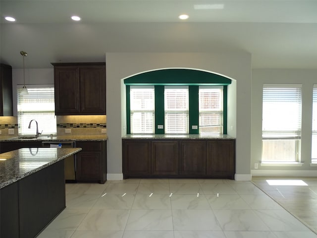 kitchen with a sink, marble finish floor, dark brown cabinets, dark stone counters, and tasteful backsplash