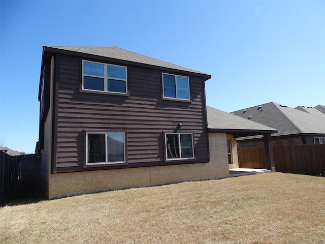 rear view of house featuring a lawn, a patio, a fenced backyard, roof with shingles, and brick siding