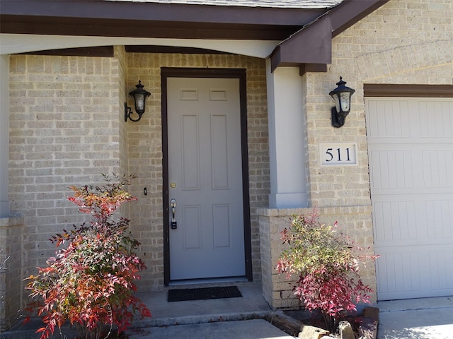 view of exterior entry with an attached garage and brick siding