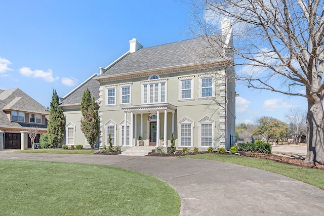 colonial home with a front yard, a chimney, and stucco siding