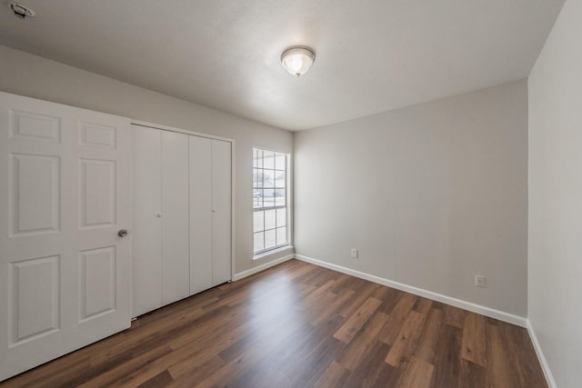 unfurnished bedroom with dark wood-style floors, baseboards, and a closet