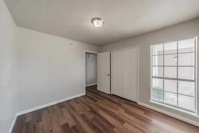 unfurnished bedroom featuring a closet, visible vents, dark wood-type flooring, and baseboards