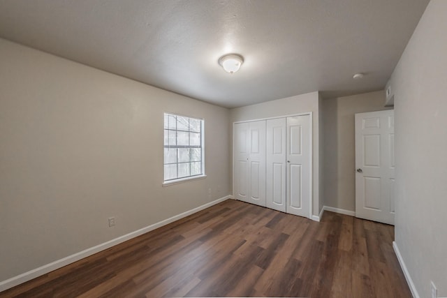 unfurnished bedroom with a closet, baseboards, and dark wood-type flooring