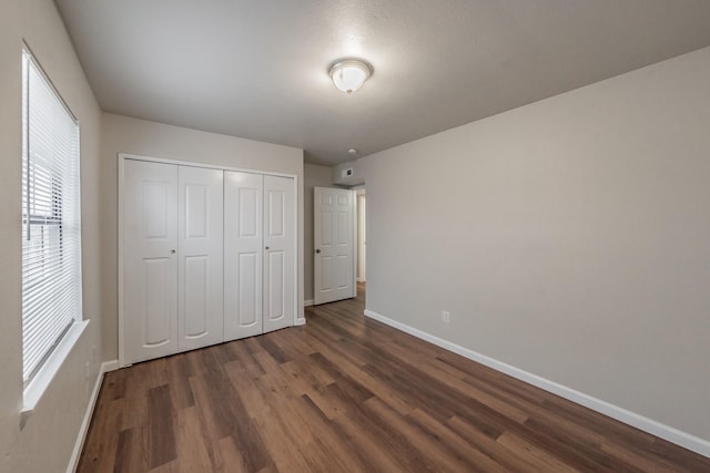 unfurnished bedroom featuring dark wood-style floors, a closet, and baseboards