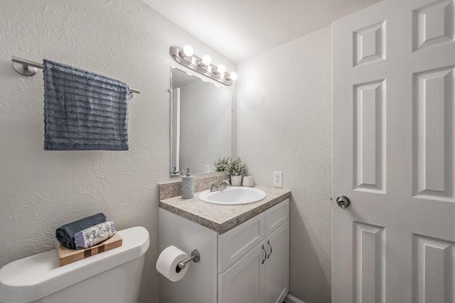 bathroom featuring toilet, vanity, and a textured wall