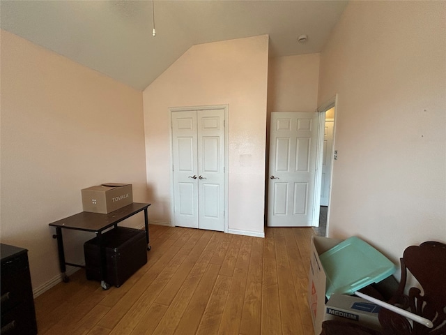 bedroom featuring a closet, baseboards, high vaulted ceiling, and hardwood / wood-style floors