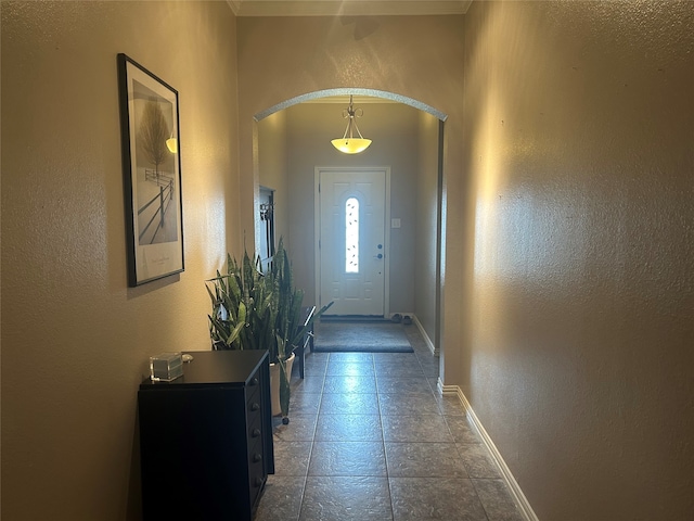 doorway to outside featuring tile patterned flooring, baseboards, arched walkways, and a textured wall