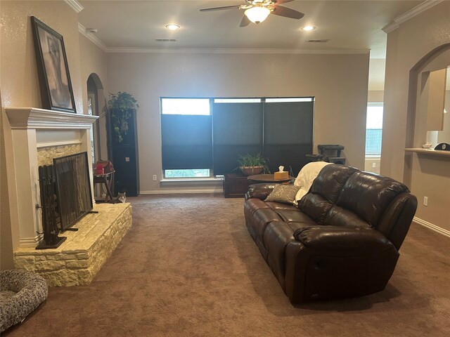 carpeted living area featuring arched walkways, a fireplace with raised hearth, crown molding, and ceiling fan