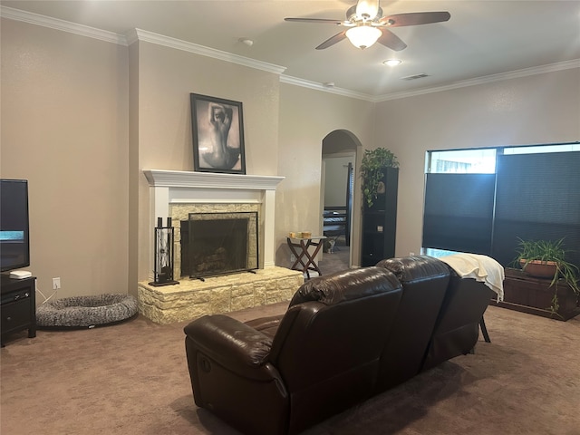 carpeted living area featuring visible vents, arched walkways, ornamental molding, a stone fireplace, and ceiling fan