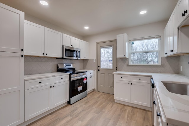 kitchen featuring light stone counters, stainless steel appliances, white cabinetry, backsplash, and light wood finished floors