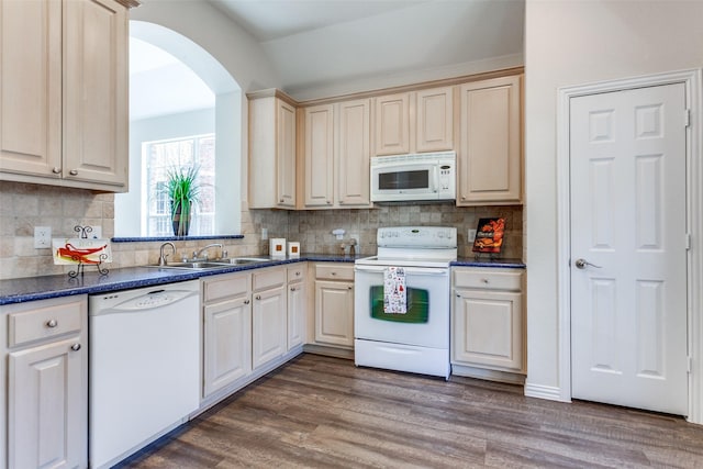 kitchen with white appliances, dark countertops, wood finished floors, and a sink