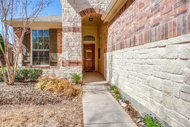 view of exterior entry with brick siding, stone siding, and a shingled roof