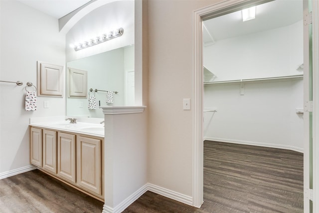 full bathroom with double vanity, a sink, baseboards, and wood finished floors