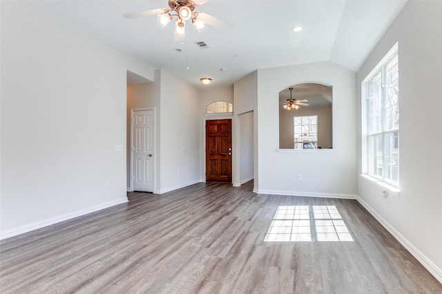 empty room with a ceiling fan, wood finished floors, visible vents, baseboards, and vaulted ceiling