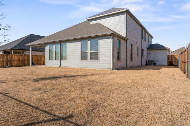 rear view of house with a fenced backyard, roof with shingles, a yard, central AC, and brick siding