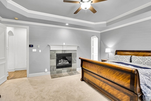 carpeted bedroom with ornamental molding, arched walkways, a tiled fireplace, and a tray ceiling