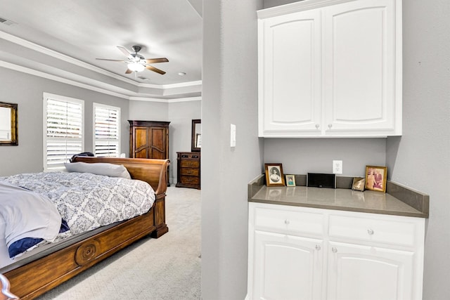 bedroom with light colored carpet, a ceiling fan, visible vents, ornamental molding, and a raised ceiling