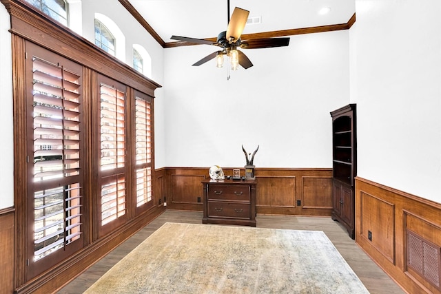 office featuring visible vents, a wainscoted wall, light wood-style flooring, ceiling fan, and crown molding