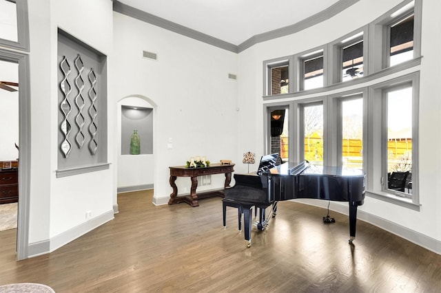 living area featuring arched walkways, visible vents, ornamental molding, wood finished floors, and baseboards