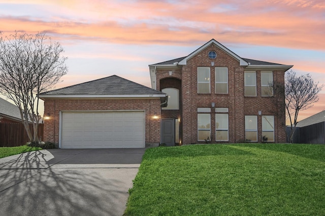 traditional home featuring a lawn, driveway, fence, an attached garage, and brick siding