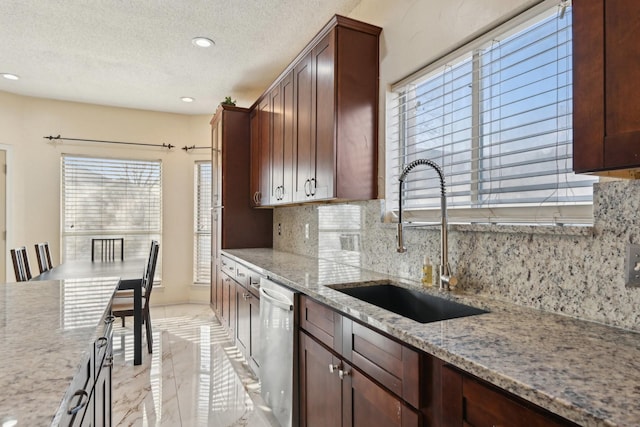 kitchen with light stone countertops, a sink, decorative backsplash, a textured ceiling, and stainless steel dishwasher