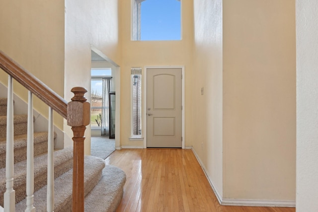 foyer with light wood-type flooring, baseboards, a towering ceiling, and stairs