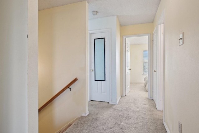 hallway featuring an upstairs landing, baseboards, and carpet