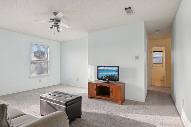 carpeted living area featuring baseboards, visible vents, a textured ceiling, and ceiling fan