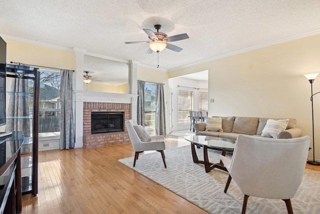 living room with a wealth of natural light, a brick fireplace, light wood-style flooring, and a ceiling fan