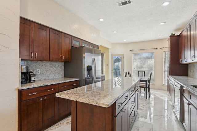 kitchen with stainless steel appliances, a textured ceiling, marble finish floor, and decorative backsplash