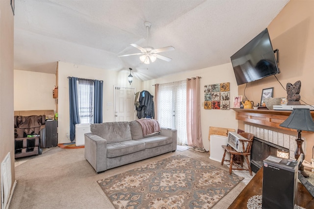 carpeted living room with a fireplace, vaulted ceiling, a ceiling fan, and a healthy amount of sunlight