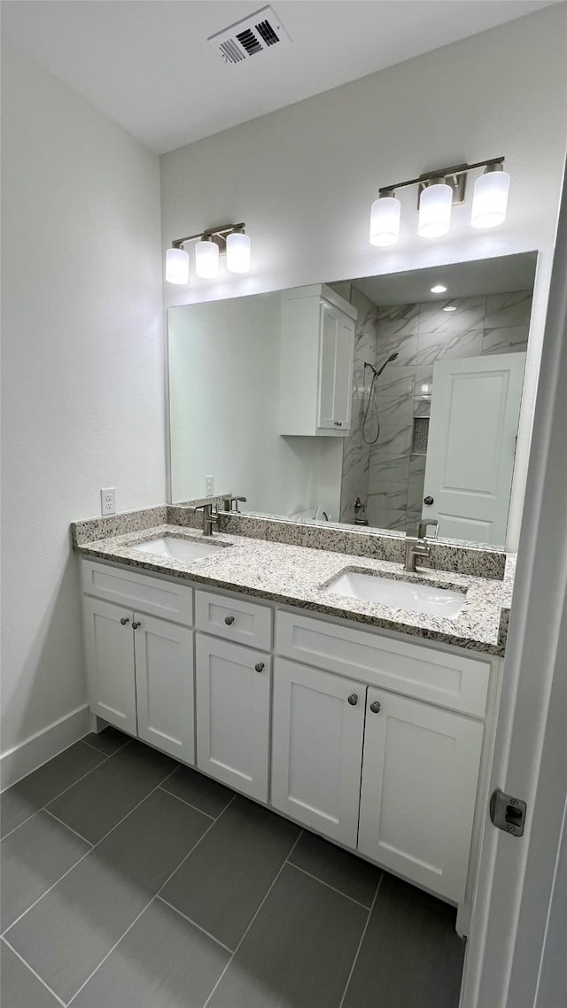 bathroom featuring a marble finish shower, double vanity, visible vents, a sink, and baseboards