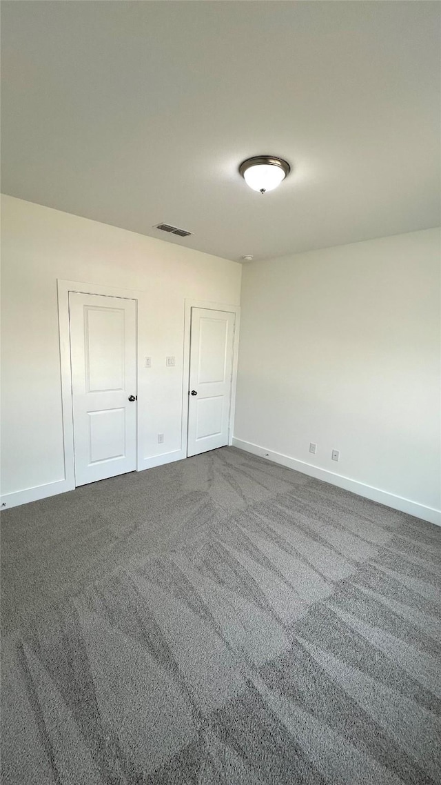 spare room featuring dark carpet and baseboards