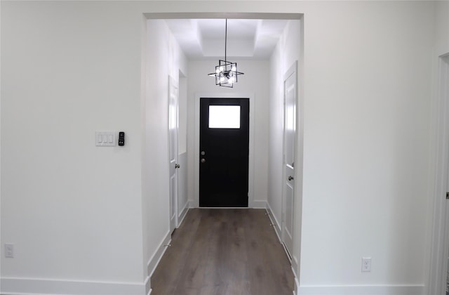 doorway with a chandelier, a raised ceiling, dark wood finished floors, and baseboards