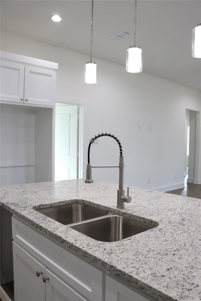 kitchen with light stone counters, a sink, visible vents, white cabinets, and hanging light fixtures