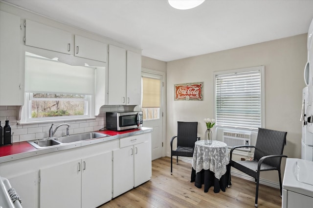 kitchen with stainless steel microwave, backsplash, white cabinetry, a sink, and light wood-type flooring