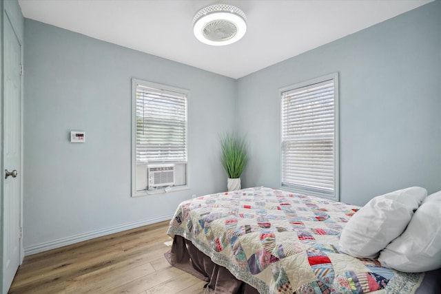 bedroom with cooling unit, multiple windows, baseboards, and wood finished floors