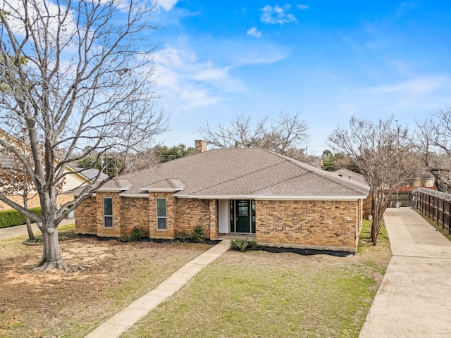 view of front of house featuring brick siding, fence, roof with shingles, a chimney, and a front yard