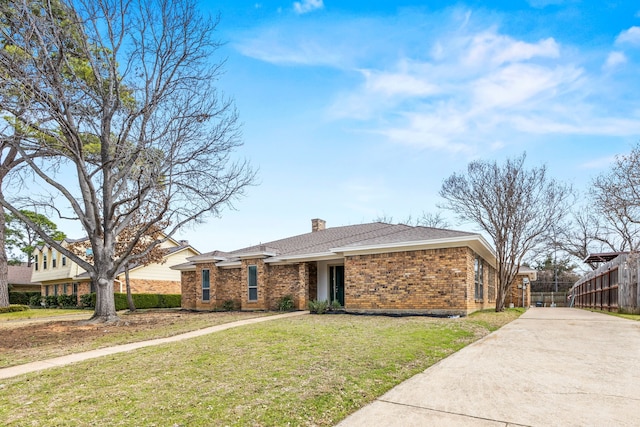 view of front of property featuring brick siding, fence, concrete driveway, a front lawn, and a chimney