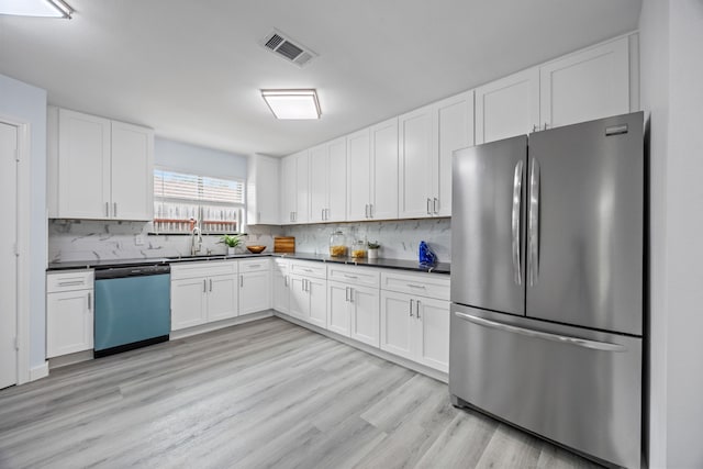 kitchen featuring visible vents, dishwasher, dark countertops, freestanding refrigerator, and a sink