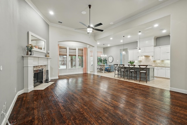 unfurnished living room featuring visible vents, ornamental molding, a stone fireplace, light wood finished floors, and ceiling fan