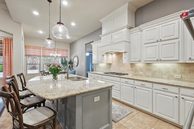 kitchen featuring a sink, backsplash, stainless steel gas cooktop, light stone counters, and a kitchen island with sink