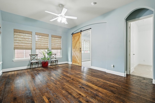 unfurnished room featuring baseboards, a ceiling fan, a barn door, and wood-type flooring