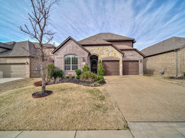 french country home featuring an attached garage, concrete driveway, brick siding, and a front yard