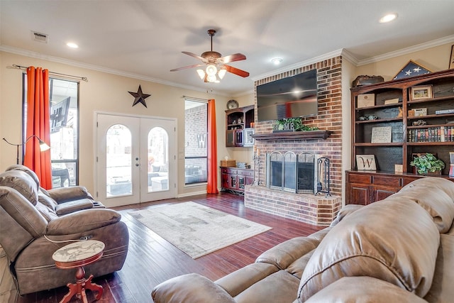 living area with wood finished floors, visible vents, ornamental molding, french doors, and a brick fireplace