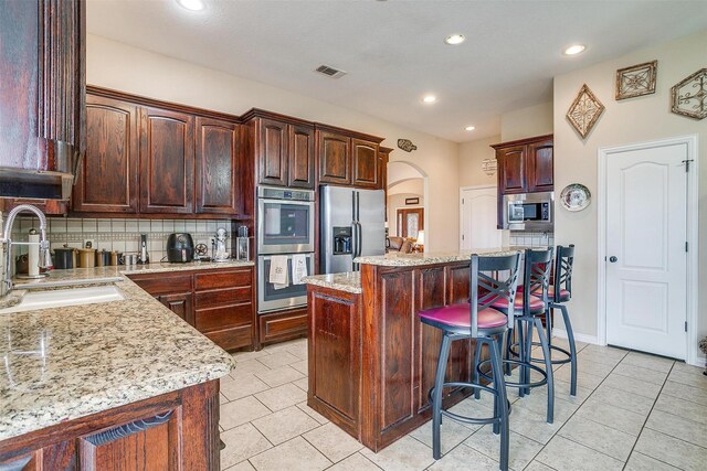 kitchen featuring arched walkways, stainless steel appliances, visible vents, backsplash, and a sink