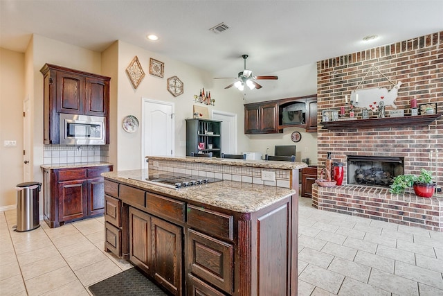 kitchen with black electric cooktop, a kitchen island, visible vents, a brick fireplace, and stainless steel microwave