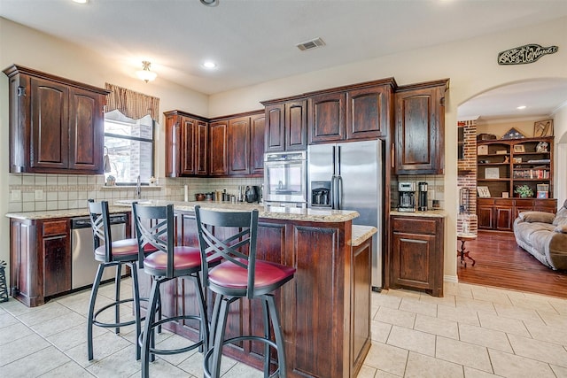 kitchen with a center island, visible vents, backsplash, appliances with stainless steel finishes, and a kitchen bar